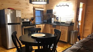 A compact kitchen with a dining table, chairs, a refrigerator, stove, microwave, and a sink. - The Retreat - Cozy studio cabin - Hot Tub, Firepit, pond, natural playground (Logan)