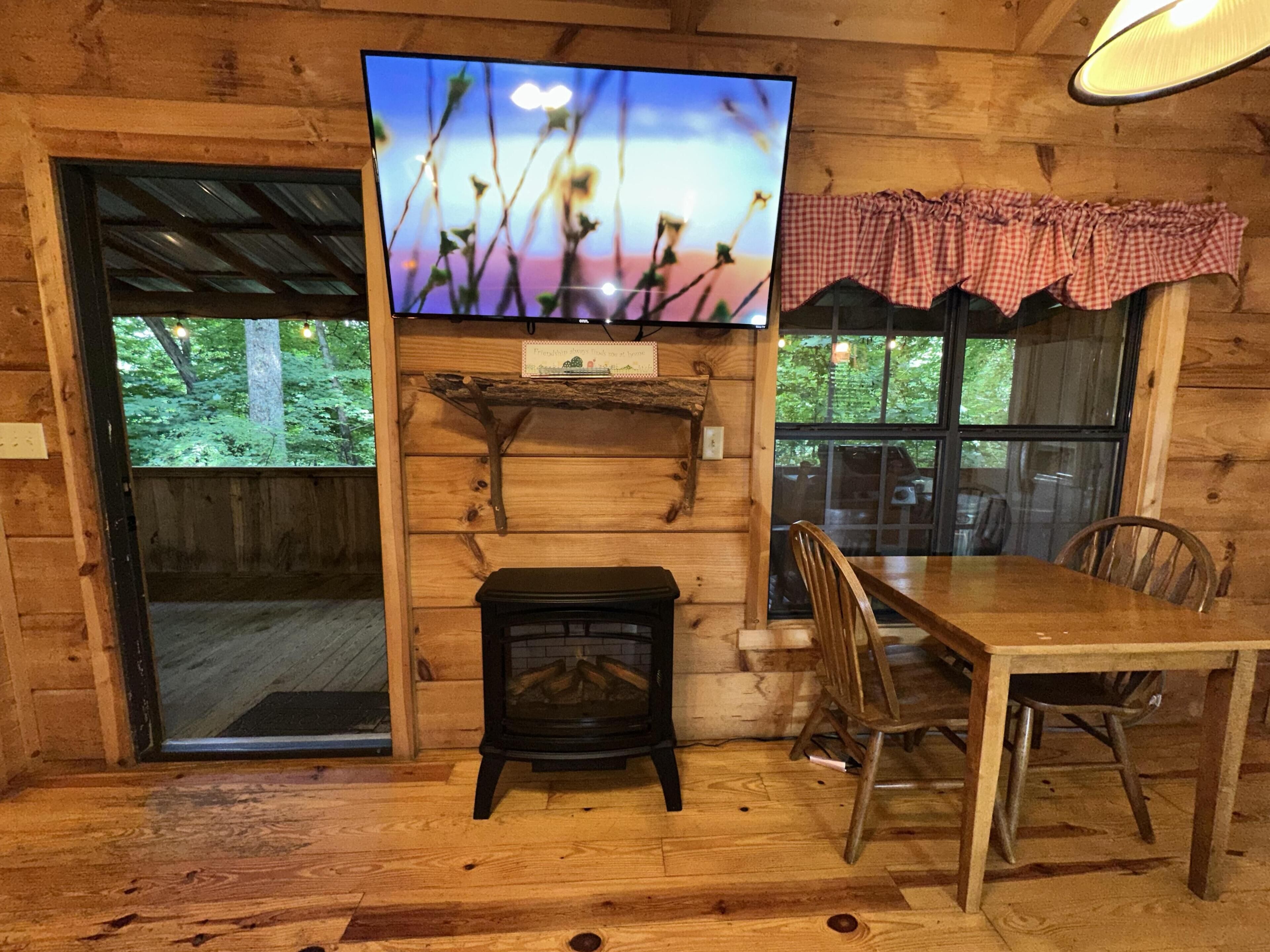 Interior de una cabaña de madera con chimenea, televisor montado en la pared, mesa de comedor y sillas.