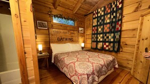 Una habitación de cabaña de madera con una cama, un colcha, un letrero que dice 'Stony Fork Lake BATHING' y un cortinón acolchado.