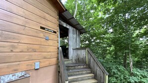 Una cabaña de madera con una escalera que conduce a un porche cubierto, rodeada por un bosque frondoso.