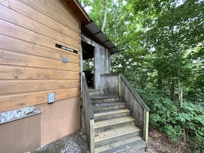 Une cabane en bois avec un escalier menant à une entrée couverte, entourée d’une forêt dense.