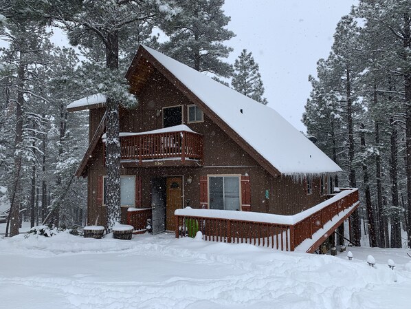 Een vakantiehuis van hout met een balkon, omgeven door met sneeuw bedekte bomen.