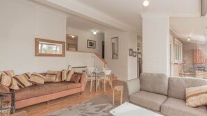Amplia sala de estar con un sofá marrón, un sofá gris y un comedor con mesa y sillas.