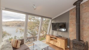 Una sala de estar moderna con un ventanal grande, un televisor de pantalla plana, un mueble de entretenimiento de madera y una chimenea.