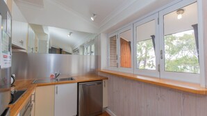 Una cocina moderna con lavavajillas de acero inoxidable, encimera de madera y ventana con vistas a árboles.