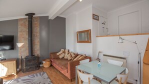 Una sala de estar acogedora con chimenea, televisor, mesa de comedor con sillas y sofá con cojines.
