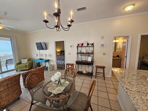 Uma sala de jantar com cadeiras de vime, uma mesa redonda, um lustre e vista para o oceano através de uma porta de correr.