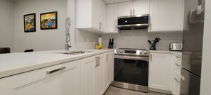 Una cocina moderna con armarios blancos, electrodomésticos de acero inoxidable y un microondas sobre la estufa.