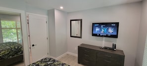Ein Schlafzimmer mit einem Bett, einer Kommode, einem an der Wand befestigten Fernseher und einer Tür.