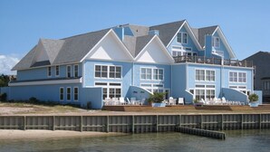 A large, two-story house with a balcony, situated by a body of water. - Waterside: Soundfront condo with spectacular sunsets. (Ocracoke)