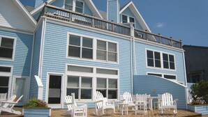 A two-story house with a balcony, multiple windows, and outdoor seating area with white chairs and tables. - Waterside: Soundfront condo with spectacular sunsets. (Ocracoke)
