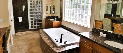 A bathroom with a large bathtub, a vanity with a sink, and a shower area.