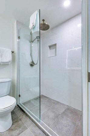 A modern bathroom with a glass-enclosed shower, a white toilet, and a small square shelf on the wall. - Greystone Lodge 310 Ski-in/Out by Acer Vacations (Whistler)