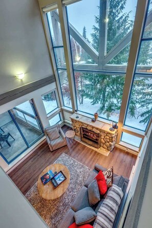 A high-ceilinged living room with a stone fireplace, large windows, and a cozy seating area.