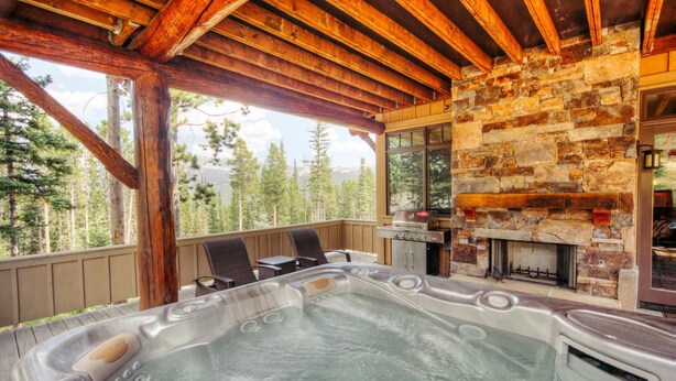 Ein Whirlpool mit Kamin aus Naturstein, einer Holzterrasse und Blick auf einen Wald.