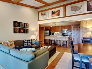 A modern living room with a sofa, a dining table with chairs, and a kitchen area with wooden cabinets and appliances.
