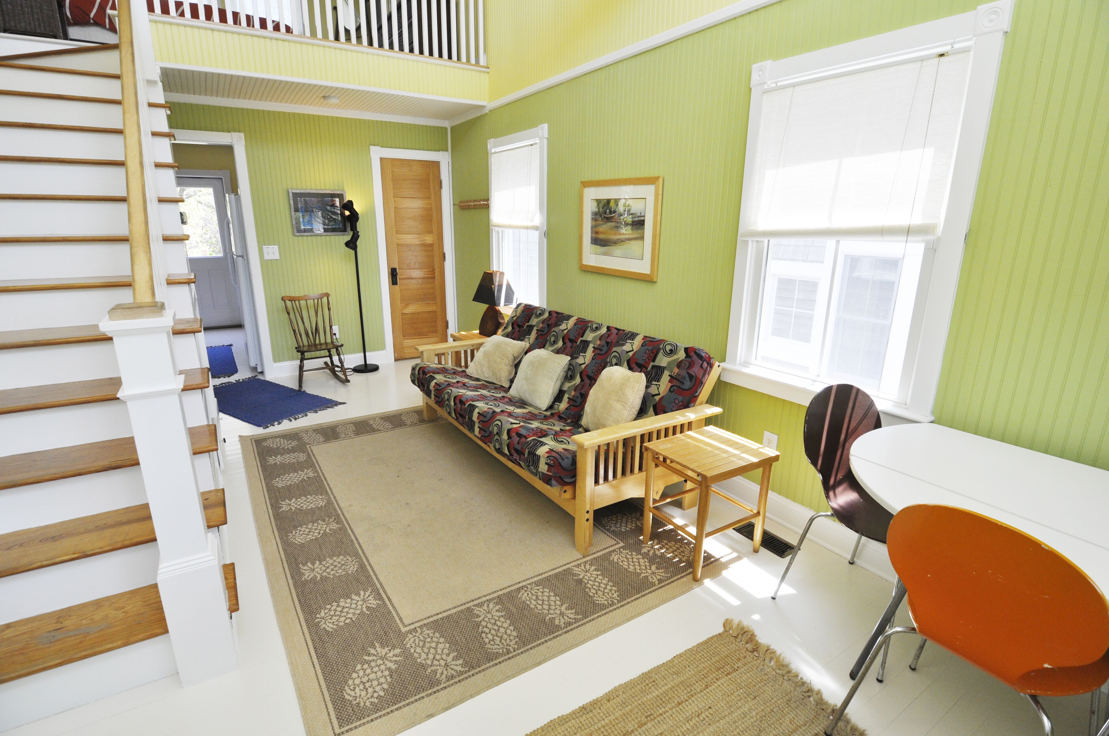 A multi-level living space with a staircase, a sofa, a dining table, and a chair.