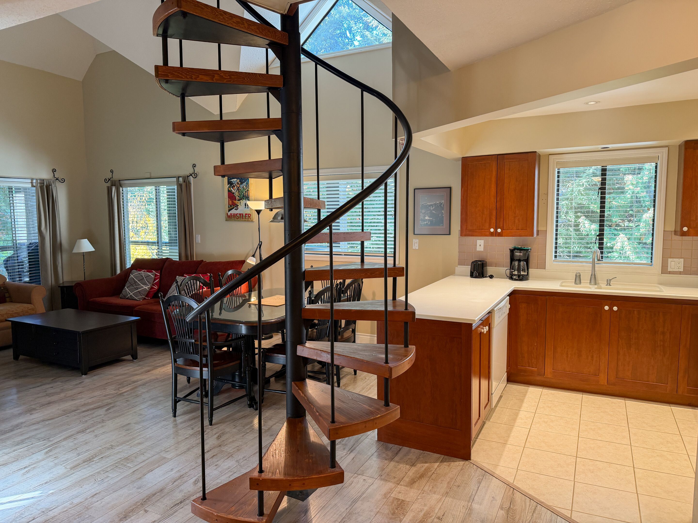 A modern living room with a spiral staircase, a dining area, and a kitchen with wooden cabinets.