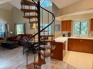 A modern living room with a spiral staircase, a dining area, and a kitchen with wooden cabinets.