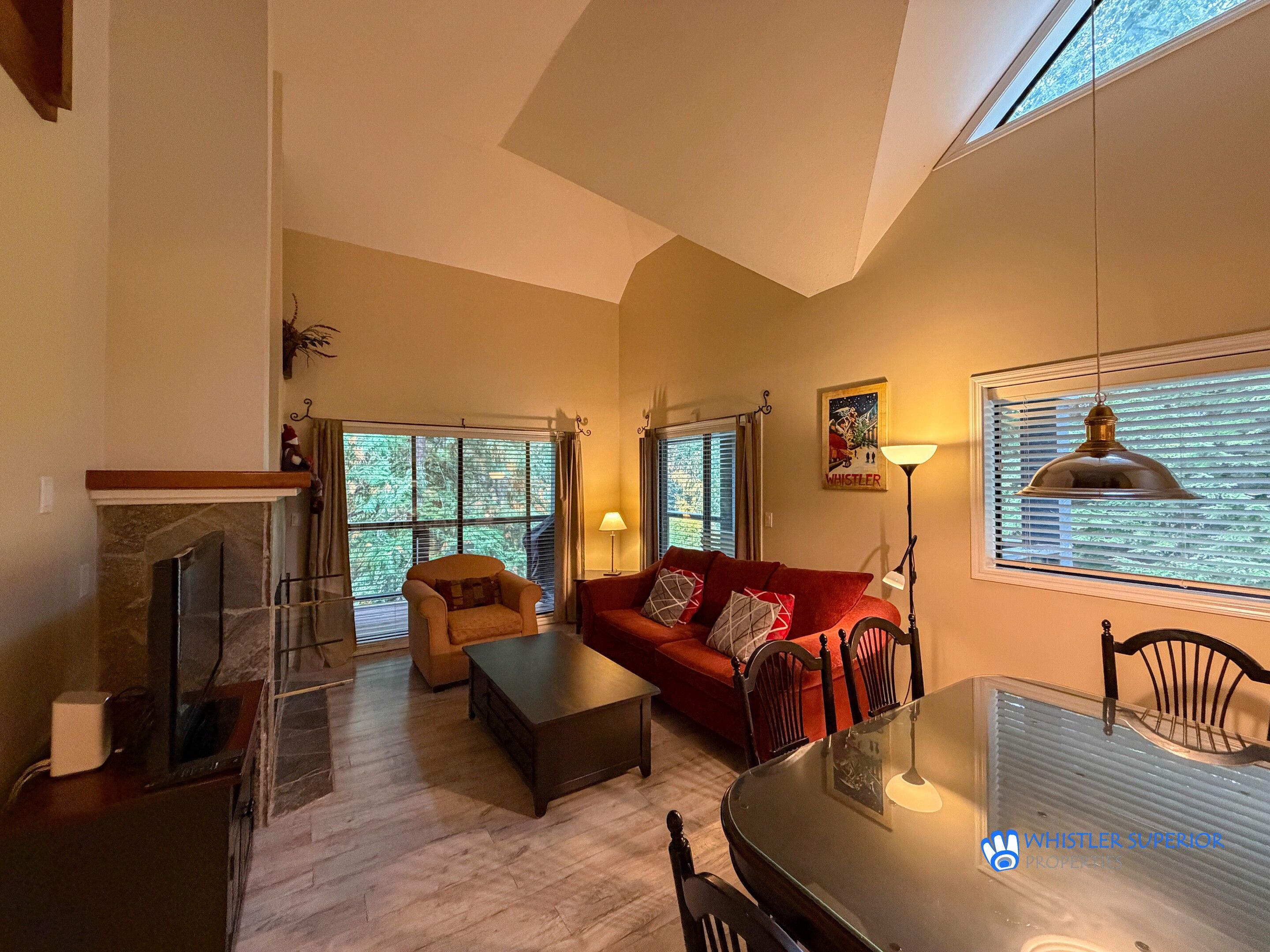 A living room with a fireplace, a red sofa, a glass coffee table, and a dining table with chairs.