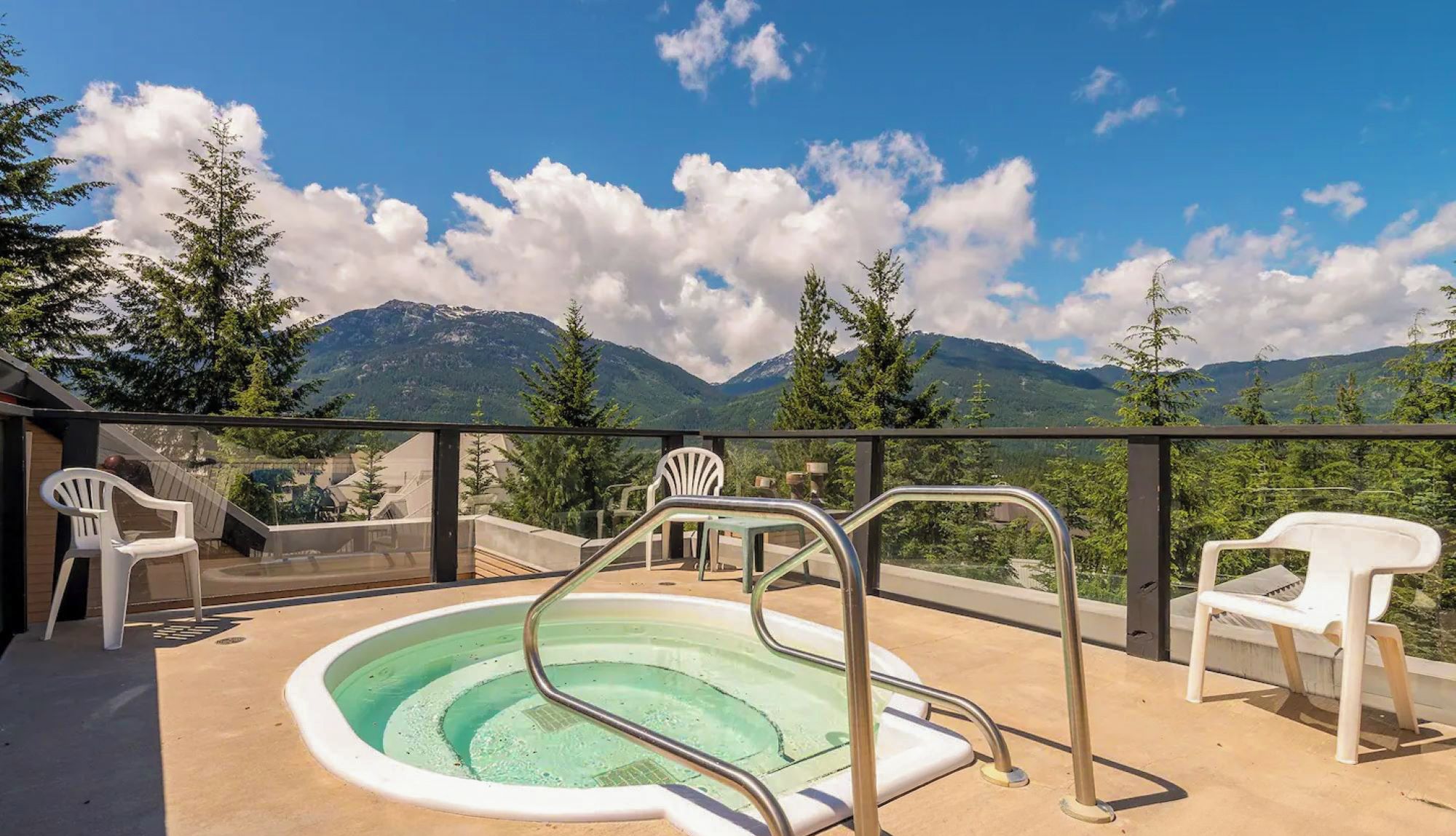 A pool area with a view of mountains, surrounded by trees and equipped with chairs and a pool ladder.