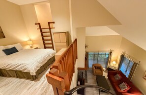 Ein Schlafzimmer mit Bett, einer Holzlade, einem Sofa und Blick ins Freie.