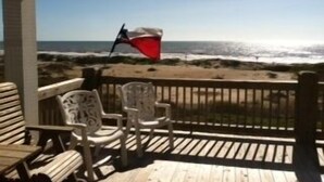 A wooden deck with two white chairs and a red flag. - Shore Haven - 2 Bedrooms, 2 Bath, Sleeps 10 - Beach Front! (Crystal Beach)
