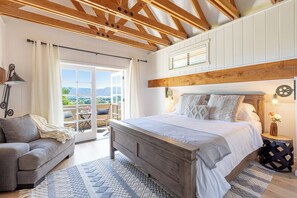 Une chambre à coucher avec un lit en bois, un canapé gris, un tapis à motifs et une vue sur l’extérieur.