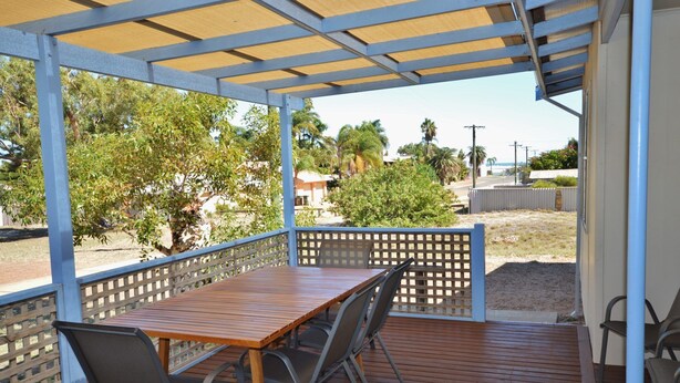 Un espacio al aire libre techado con una mesa y sillas de madera, vistas del paisaje circundante y una cerca.
