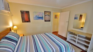 Un dormitorio con cama, mesita de noche, lámpara, cómoda y espejo. Hay tres carteles en la pared.