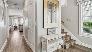 A hallway with a white console table, a welcome sign, and a mirror. - Liberty Sky: Private Pool, Water Park, Golf View, Near Disney (Kissimmee)