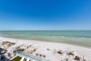 A beach view with a clear sky, sandy beach, and a few lounge chairs.