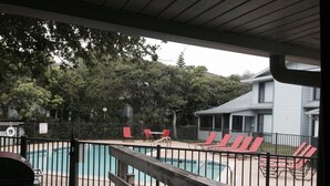 A wooden deck with a pool and red chairs. - Back patio overlooking community pool and walk to the beach (New Smyrna Beach)