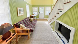 A room with a patterned sofa, a television, and a staircase. - Secret Cedars: Soundfront, perfect kayaking or water activities. (Ocracoke)