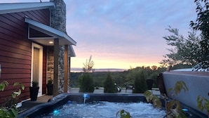 A hot tub with a stone chimney, surrounded by potted plants, and a view of the sunset. - The PearTree Cottage- enjoy the view in the hot tub! 10 minutes from Berlin (Dundee)
