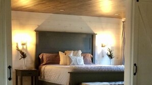 A cozy bedroom with a bed, bedside tables, and a nightstand. There is a chair and a table with a candle and greenery. - The PearTree Cottage- enjoy the view in the hot tub! 10 minutes from Berlin (Dundee)
