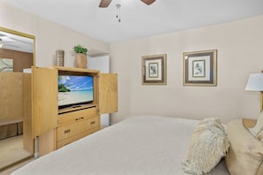 Een slaapkamer met een bed, een houten tv-meubel met een televisie, een plafondventilator en ingelijste foto's aan de muur.