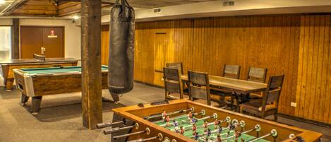 A room with a foosball table, pool table, and a punching bag.