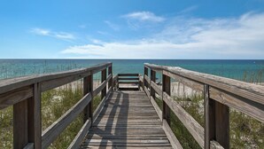 A wooden boardwalk leading to a beach with clear blue water and a partly cloudy sky. - “Dolphin Watch” Amazing Gulf Front Home, Elevator, Paddleboard! (Navarre Beach)