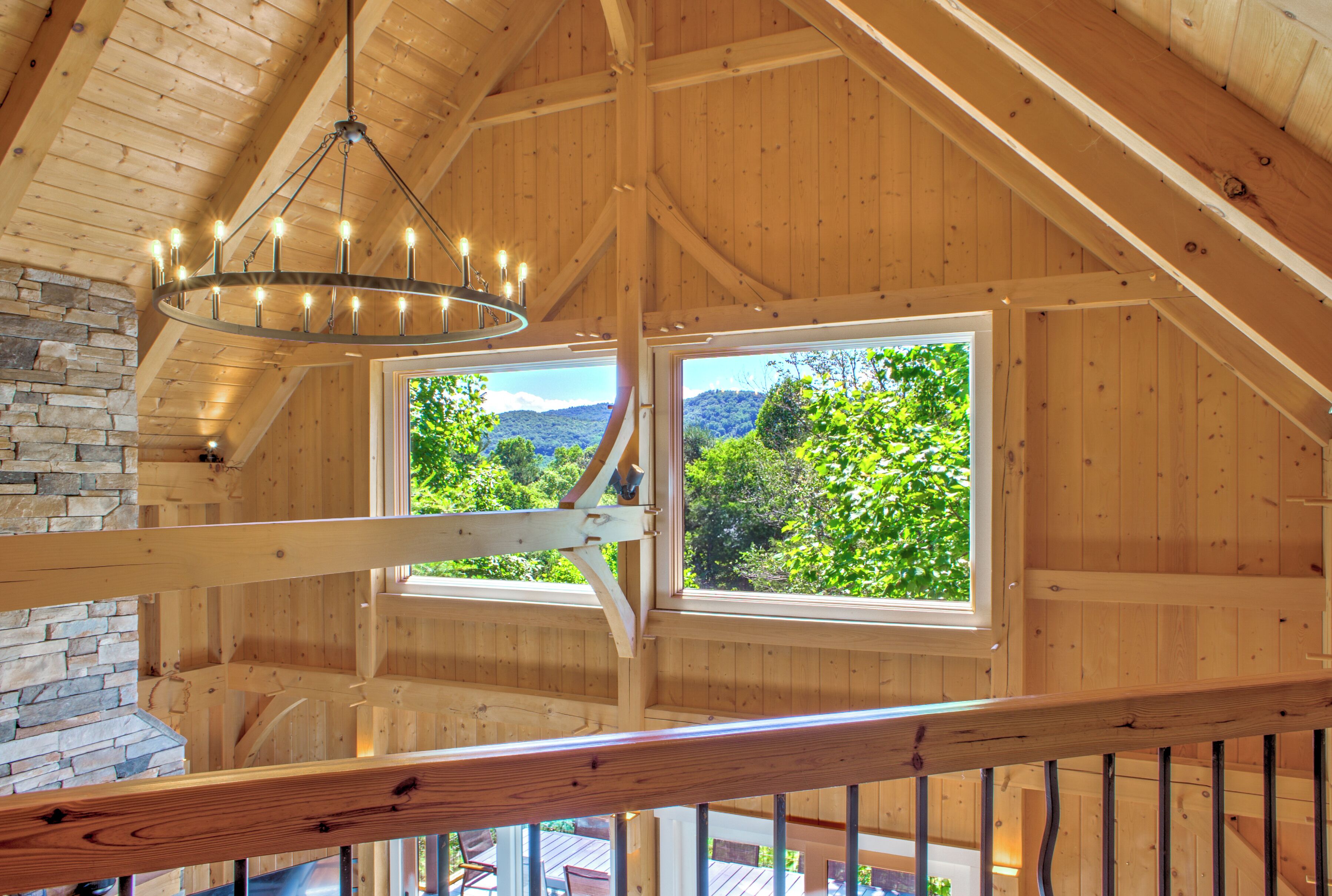 A wooden interior with a stone wall, a chandelier, and two windows offering a view of greenery.
