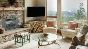 A cozy living room with a stone fireplace, a flat-screen TV, comfortable seating, and a large window offering a scenic view. - Steps to Six Shooter Lift Access | Views (Big Sky)