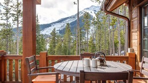 A wooden deck with a round table and chairs, overlooking a snowy mountain and forest. - Steps to Six Shooter Lift Access | Views (Big Sky)
