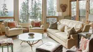 A cozy living room with a large window, a sofa, two armchairs, a glass coffee table, and a leather ottoman. - Steps to Six Shooter Lift Access | Views (Big Sky)
