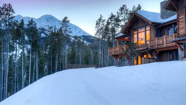 A log cabin with a balcony, surrounded by snow-covered ground and tall pine trees, with mountains in the background. - Steps to Six Shooter Lift Access | Views (Big Sky)
