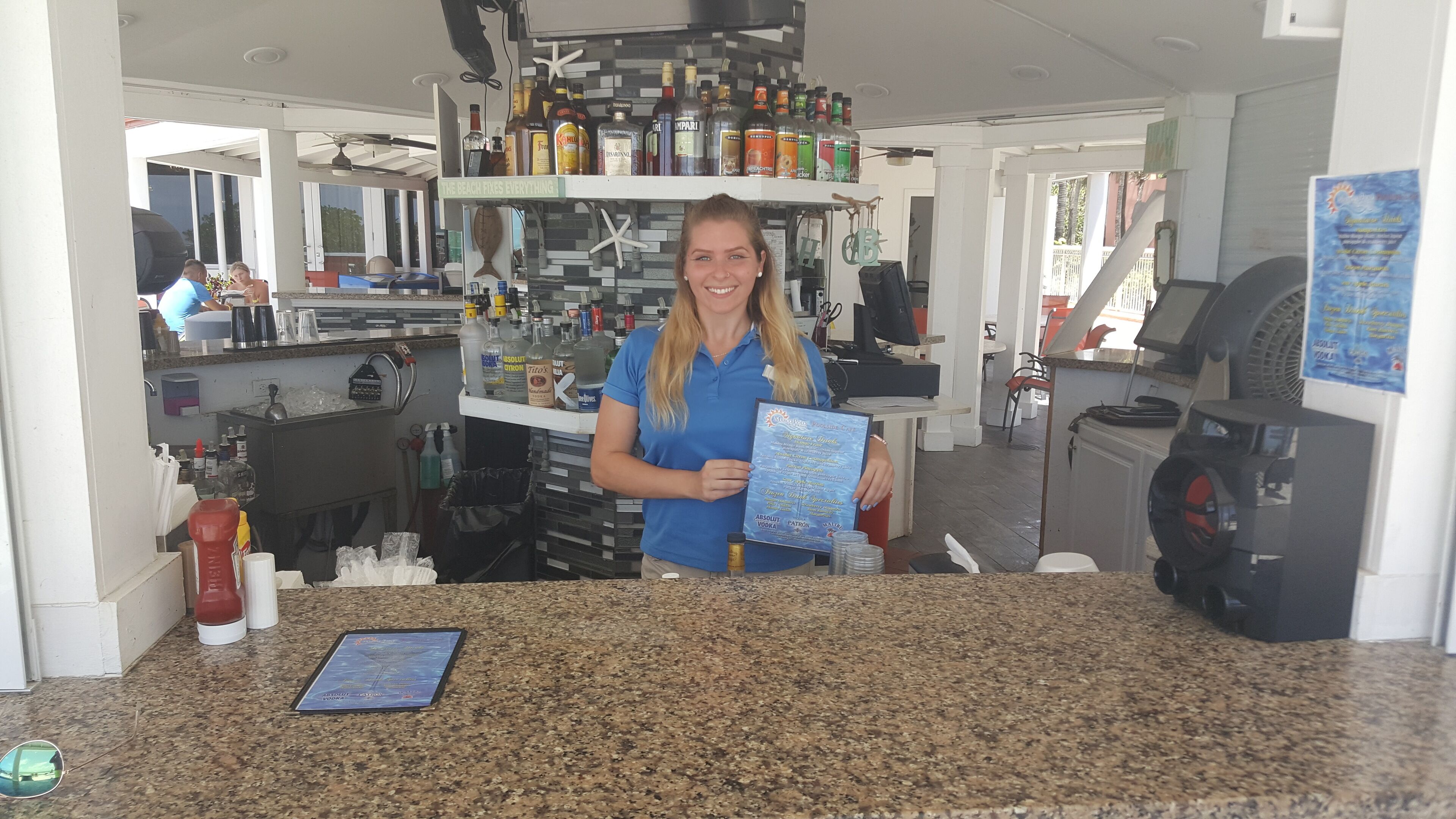 Une cuisine dotée d’un plan de travail en granit, de divers appareils électroménagers et d’un coin bar avec des bouteilles et un panneau indicateur.