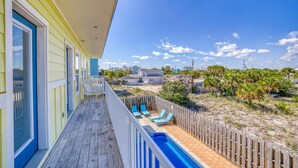 Un balcón con piscina, terraza de madera y vistas a casas y vegetación.