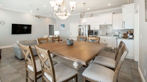 Una cocina moderna con gabinetes blancos, un refrigerador de acero inoxidable y un comedor con mesa de madera y sillas tapizadas.