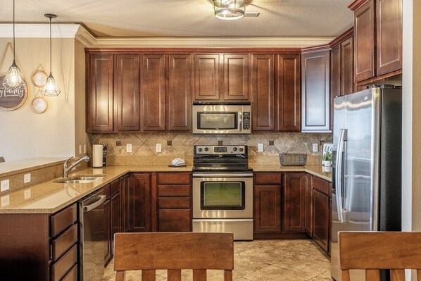 A kitchen with wooden cabinets, a stainless steel refrigerator, a microwave, an oven, and a sink.