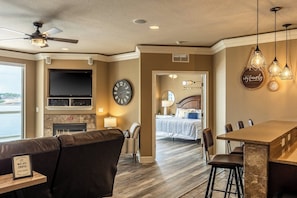 A living room with a TV, fireplace, clock, and a dining area with bar stools.