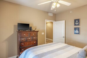 Un dormitorio con cama, cómoda, televisor, ventilador de techo y decoración náutica en las paredes.